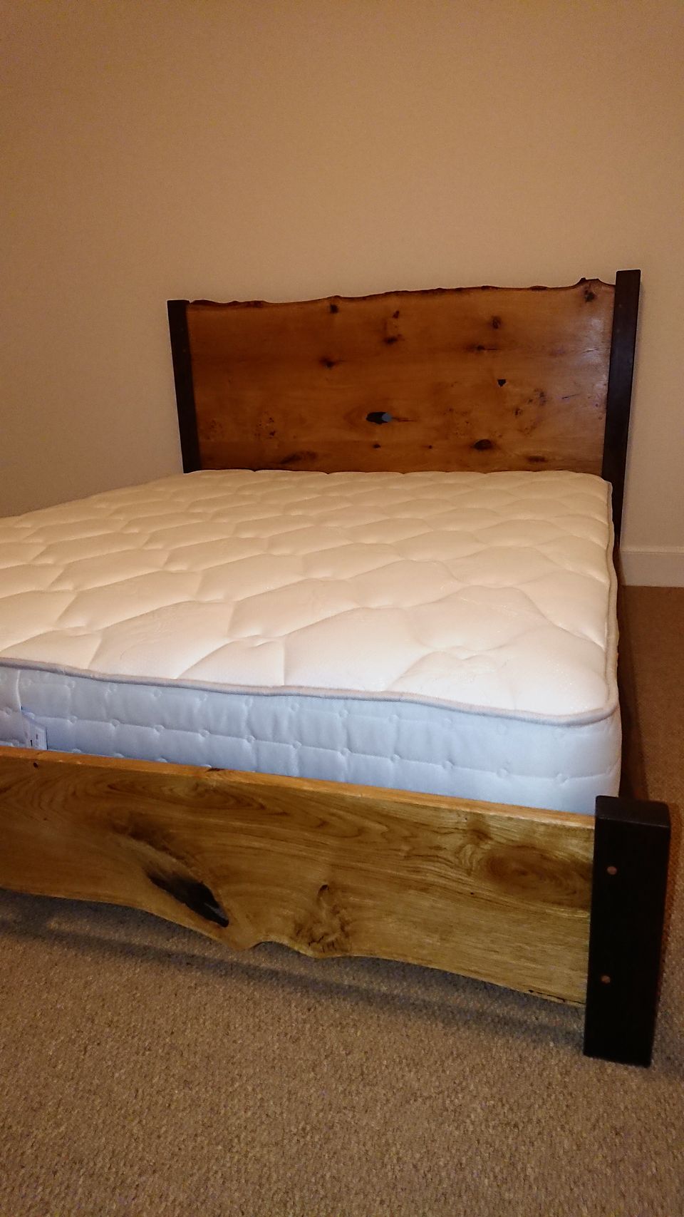 Bed frame with a live-edge headboard and figured side rails, with mattress fitted