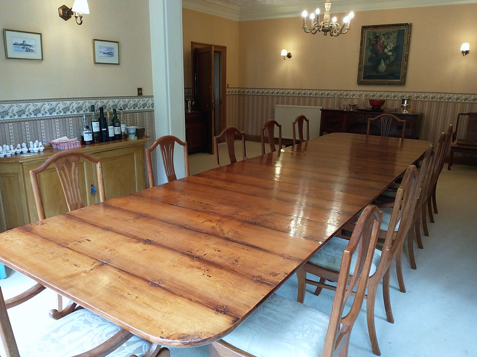Long polished plank-top extending dining table with shield-back chairs in a dining room with wall lights and a chandelier