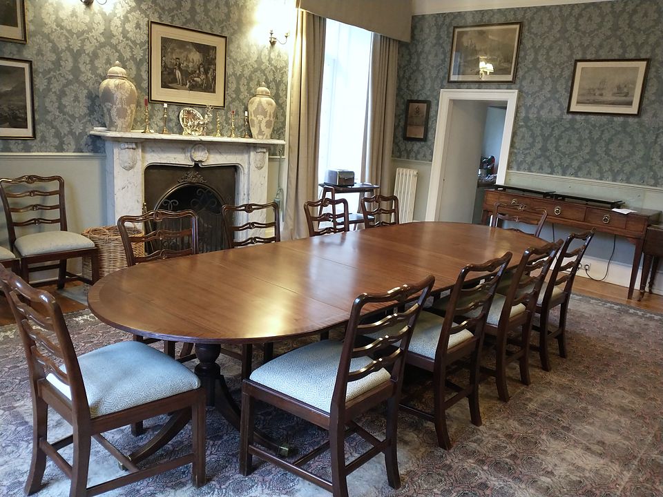 Wide view of a restored extending dining table and ladder-back chairs in front of a marble fireplace